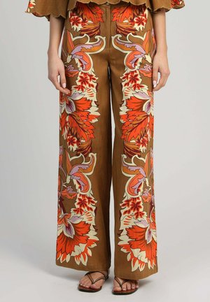 Pantalon marron à jambes larges avec de grands motifs floraux vibrants orange, violet et crème, porté avec des sandales marron à brides.