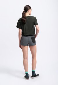 Donkergroene shirt met korte mouwen, grijze shorts met opgerolde randen, zwarte achterzakaccent, gecombineerd met zwarte sneakers en teal sokken.
