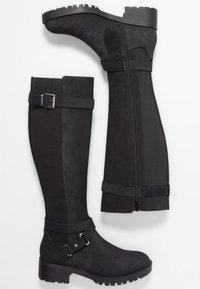 Bottes noires montantes jusqu'au genou avec talons épais, fermeture éclair latérale et boucles décoratives, vues de profil et de dos sur fond blanc.