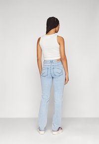 Ljust blå denim, utsvängda jeans med medelhög midja, bakfickor som har en unik stickningsdesign, kombinerade med en åtsittande vit tanktop.