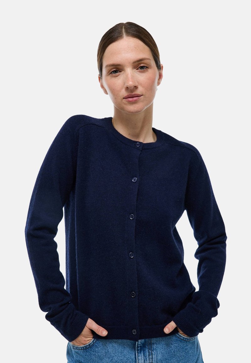 Cardigan bleu marine en tissu doux, avec un col rond et une fermeture à boutons, doté de poignets côtelés et d'une coupe décontractée.