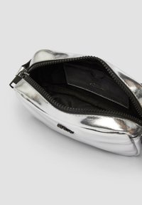Silberne metallische Tasche mit glatter Textur, runder Form und schwarzem Innenraum. Verfügt über einen Reißverschluss und eine kleine Innentasche.