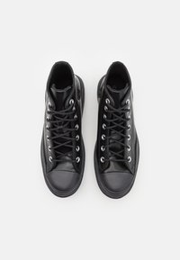 Coppia di sneakers nere alte con lacci, occhielli in metallo e suole in gomma su sfondo bianco, viste dall'alto.