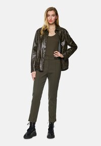 Shiny dark green leopard-print faux leather shirt jacket, olive green tank top, olive tailored pants, and black platform lace-up boots.