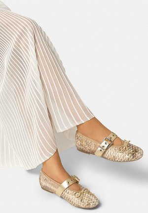 Pies con bailarinas doradas de estampado de piel de serpiente con tiras con hebillas, combinadas con pantalones anchos plisados blancos.