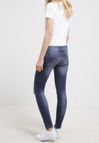 Jean skinny en denim bleu foncé, avec une coupe slim et un léger effet délavé. À associer avec des baskets blanches et un t-shirt blanc uni.