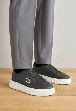 Sneakers in pelle nera con suola in gomma bianca strutturata, dotati di un accento geometrico di lato e design classico con lacci.