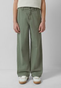 Jasnozielone, szerokie spodnie z wysokim stanem, przednimi kieszeniami i zapięciem na guzik. W połączeniu z białymi sneakersami na brązowych podeszwach.