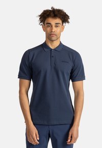Námořnická modrá polo tričko vyrobené z hladké tkaniny, které se vyznačuje klasickým límečkem, dvěma knoflíky, krátkými rukávy a logem na levé hrudi.