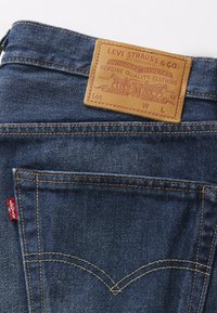 Jeans in denim blu scuro con una tasca cucita con un prominente etichetta rossa Levi's e una toppa in pelle color cuoio che mostra i dettagli del marchio.