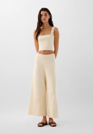 Haut court crème avec décolleté carré et accents de boutons, associé à un pantalon à jambes larges avec des motifs texturés et une finition en tricot doux.