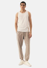 White sleeveless tank top, light grey sweatpants with cuffs, worn with cream sneakers. Pants have a relaxed fit and drawstring waist.