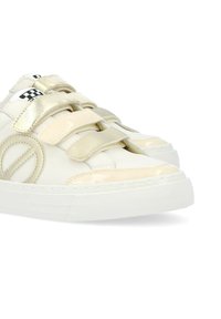 White and beige sneakers with a shiny finish, featuring Velcro straps, rounded toe, and a textured rubber sole. Checkered detail on the tongue.