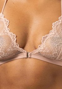 Kant bralette in zacht beige met bloemenpatroon, met gegolfde randen en een sluiting aan de voorkant. De bandjes zijn slank en verstelbaar.