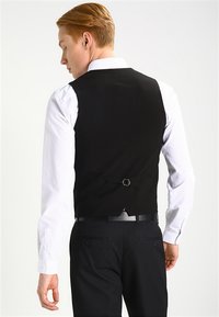 Schwarze Weste mit einer glatten Textur, verstellbarem Rückengurt, kombiniert mit einem hellen Polka-Dot-Hemd. Geeignet für formelle Anlässe.