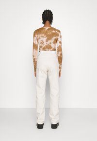 Camisola de manga longa em padrão tie-dye castanho, combinada com calças de cintura alta em off-white, com bolsos e pernas ajustadas. Botas de cano curto pretas mostradas.