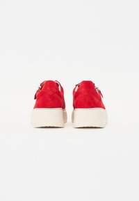 Rote Wildleder-Sneaker mit einer weißen Plateausohle, ausgestattet mit metallischem Zubehör und Schnürsenkeln. Das Design betont eine elegante, minimalistische Silhouette.