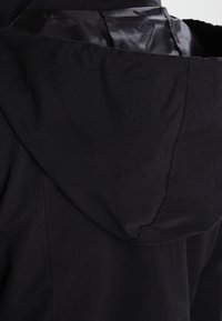 Svart huvtröja med ett slätt, matt yttertyg och ett lätt glänsande foder, med en enkel design och rena sömmar.