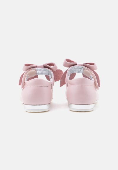Paire de chaussons roses pour bébé avec des nœuds à l’arrière et des détails argentés sur fond blanc vus de dos.