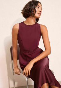 Bordó ruha testéhez simuló felsőrésszel és bővülő aljrésszel. Finom, könnyű anyagból készült. Derékszíjjal, téglalap alakú csattal díszítve.