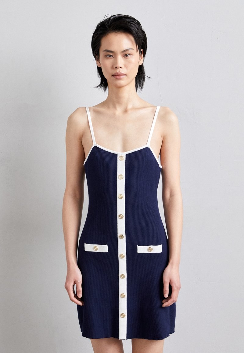 Vestido de punto navy con acentos blancos, con tirantes finos, un frente abotonado y dos bolsillos frontales con botones decorativos.
