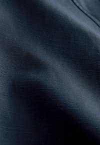 Tume mereva sinine kangas, millel on peen kootud tekstuur ja pehmed voldid, mis loovad valguse ja varju varieeruvusi.