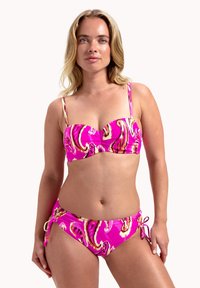 Set di bikini rosa con un motivo vorticoso in oro e bianco. La parte superiore presenta spalline sottili e un design a bandeau, mentre la parte inferiore ha lati regolabili con lacci.