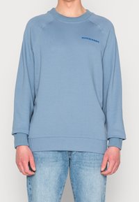 Modrá mikina s žebrovanými manžetami a spodním lemem, s kulatým výstřihem a raglánovými rukávy. Logo "SCOTCH & SODA" v kontrastní modré barvě. Měkká textura.