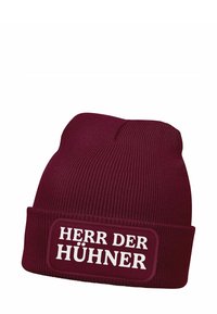 Burgundy knit beanie with ribbed texture and a folded cuff featuring a rectangular patch with white text reading "HERR DER HÜHNER."