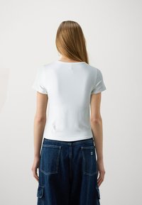 Hvit kortermet topp med rund hals, glatt tekstur. Kombinert med blå denim cargo-bukser med store lommer og sømdetaljer.