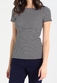 Haut à manches courtes noir et blanc rayé avec un col rond ; design ajusté en tissu doux et extensible. Accompagné de pantalons navy.