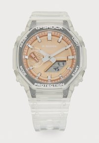 Montre G-SHOCK avec un boîtier et un bracelet en résine transparente, cadran couleur or rose, accents argentés, affichage numérique et éléments de protection.
