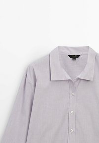 Chemise boutonnée à manches longues de couleur violet clair avec col, trois boutons blancs visibles, présentée à plat sur fond blanc.