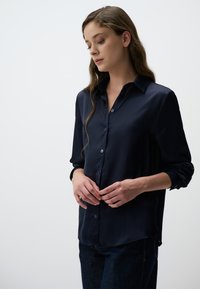 Navyblauwe zijden shirt met een knoopsluiting aan de voorkant, lange mouwen en een iets relaxte pasvorm. Soepele textuur met een subtiele glans.