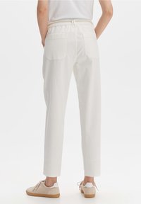 Witte katoenen broek met een relaxte pasvorm, elastische tailleband, twee achterzakken, en gecombineerd met beige sneakers. Glad oppervlak, rechte vorm.