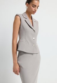 Hellgrauer taillierter Blazer mit schlanker Passform, Reverskragen und silbernen Knöpfen, kombiniert mit einem passenden Bleistiftrock. Glatte Textur.