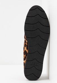 Semelle de chaussure avec un motif de bande de roulement noir et un tissu à imprimé léopard sur le côté, sur fond blanc.