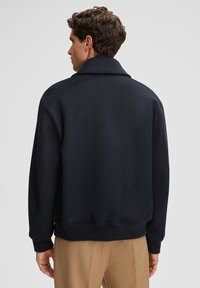 Black fleece jacket with a wide collar, relaxed fit, and ribbed cuffs. Smooth texture, minimal design, suitable for casual wear.