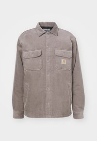 Graue Cordjacke mit durchgehendem Knopfverschluss, zwei Brusttaschen und einem kleinen Logo-Patch auf der linken Tasche.