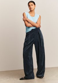 Lichtblauwe gebreide mouwloze top, gecombineerd met donker corduroy wijde broek. De broek heeft een gestructureerde afwerking en een ontspannen silhouet.