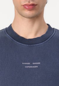 Felpa in cotone blu navy con collo a girocollo a coste. Presenta la scritta bianca "SAMSØE SAMSØE COPENHAGEN" in un design centrato e sobrio.