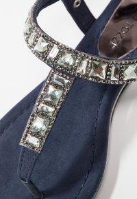 Sandale bleu marine avec bride en T ornée de strass clairs carrés et rectangulaires ainsi que de petites pierres rondes le long des bords.