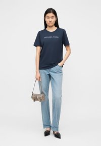 Κοντομάνικη μπλούζα σε ναυτικό μπλε με το λογότυπο "MICHAEL KORS", συνδυασμένη με ανοιχτό μπλε παντελόνι φαρδιάς γραμμής και μεταλλική τσάντα. Μαύρες γόβες με μυτερή μύτη.