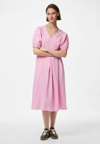 Roza karo midi haljina s napučenim rukavima, V-izrezom i nabranim strukom, u kombinaciji s tamnosmešnim patikama koje imaju bele vezice.