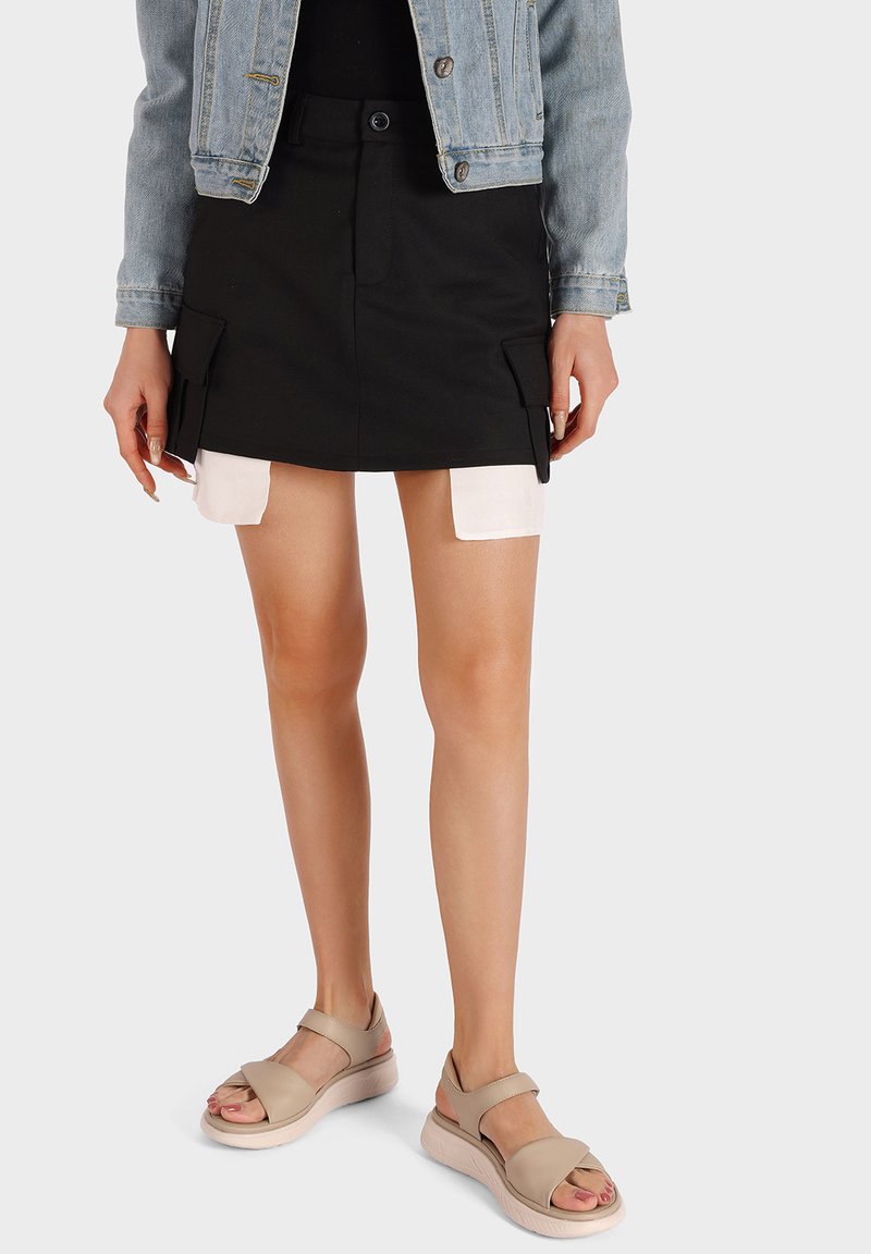 Mini gonna nera in cotone con tasche laterali, abbinata a sandali con zeppa beige con design a fascia incrociata e suola in gomma. Giacca di jeans sopra.