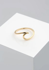 Goldener Metallring mit wellenförmigem Design, einer glatten, polierten Oberfläche und offener Form. Das Detail weist eine leichte Kurve auf.