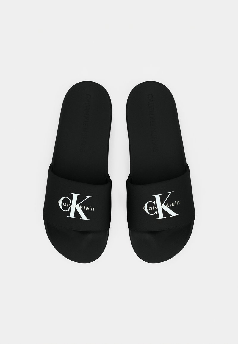 Sandales à glissière noires avec une sangle synthétique lisse. Arborent les logos blancs "Calvin Klein" et "CK". Semelle intérieure texturée pour une meilleure adhérence.