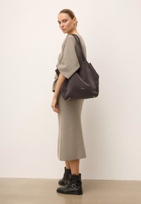 Sötét szürke vászontáska, puha anyagból, minimalista dizájnnal, arany kiegészítőkkel és strapabíró pántokkal a könnyű hordozásért.