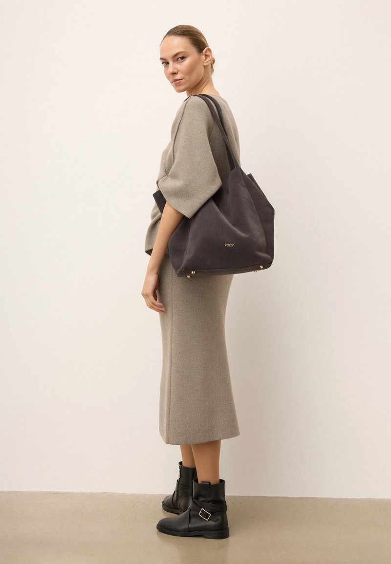 Sötét szürke vászontáska, puha anyagból, minimalista dizájnnal, arany kiegészítőkkel és strapabíró pántokkal a könnyű hordozásért.