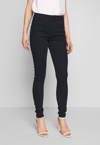 Tmavě modré skinny jeans vyrobené z denimové látky, s předními kapsami, zipovým zapínáním na knoflík a štíhlým, těsně padnoucím střihem.